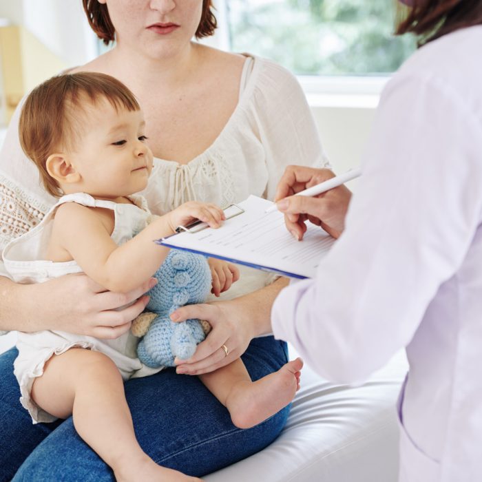 Curious little girl looking at medical history that pediatrician filling when talking to her mother
